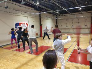 A group of adult fencers practices footwork