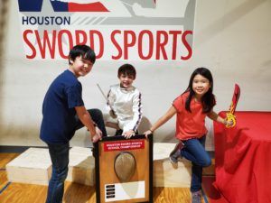 The Saint Constantine School won the Golden Mask trophy this year. Three TSCS fencers pose with the trophy after the result is announced.